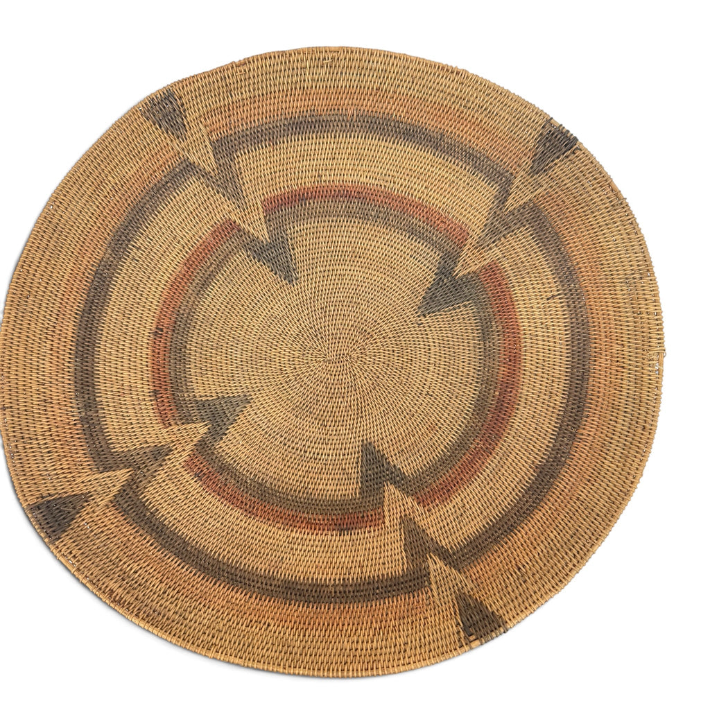 A round woven basket rug with a Southwestern geometric pattern in natural tan, brown, and reddish-brown on a white background.
