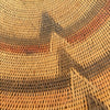 Close-up of a woven basket or mat with a geometric pattern in natural tan, brown, and muted orange tones.