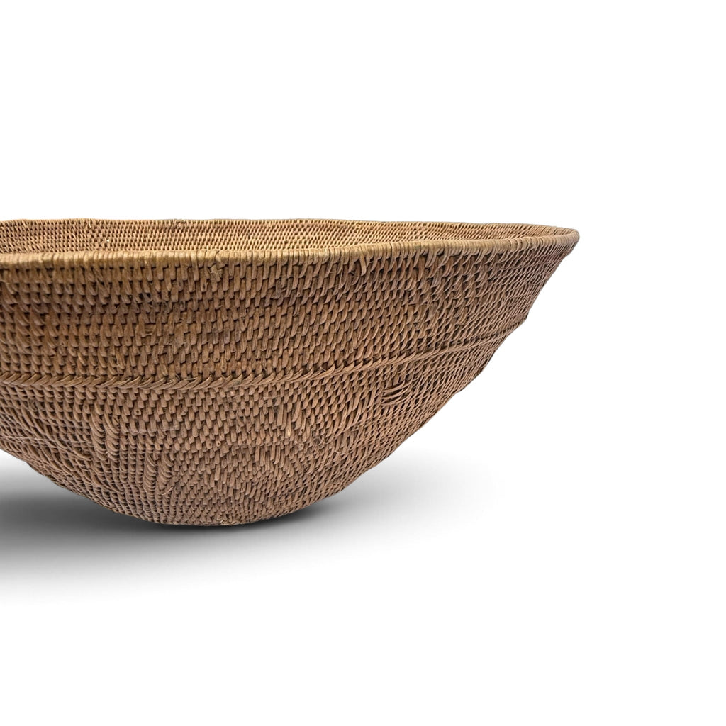 A close-up of a hand-woven natural fiber basket bowl, showcasing its detailed woven texture and warm brown color, set against a plain white background.