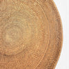 A close-up of a round woven natural fiber plate or tray, showing the detailed radial pattern of the wicker on a white background.
