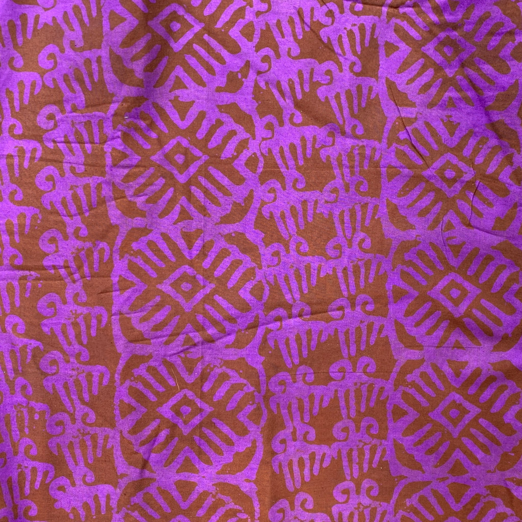 The African Fabric Wax Batik #945 features bold purple geometric and abstract tribal patterns hand stamped on reddish-brown cotton fabric with a slightly wrinkled batik texture for a striking, eye-catching design.